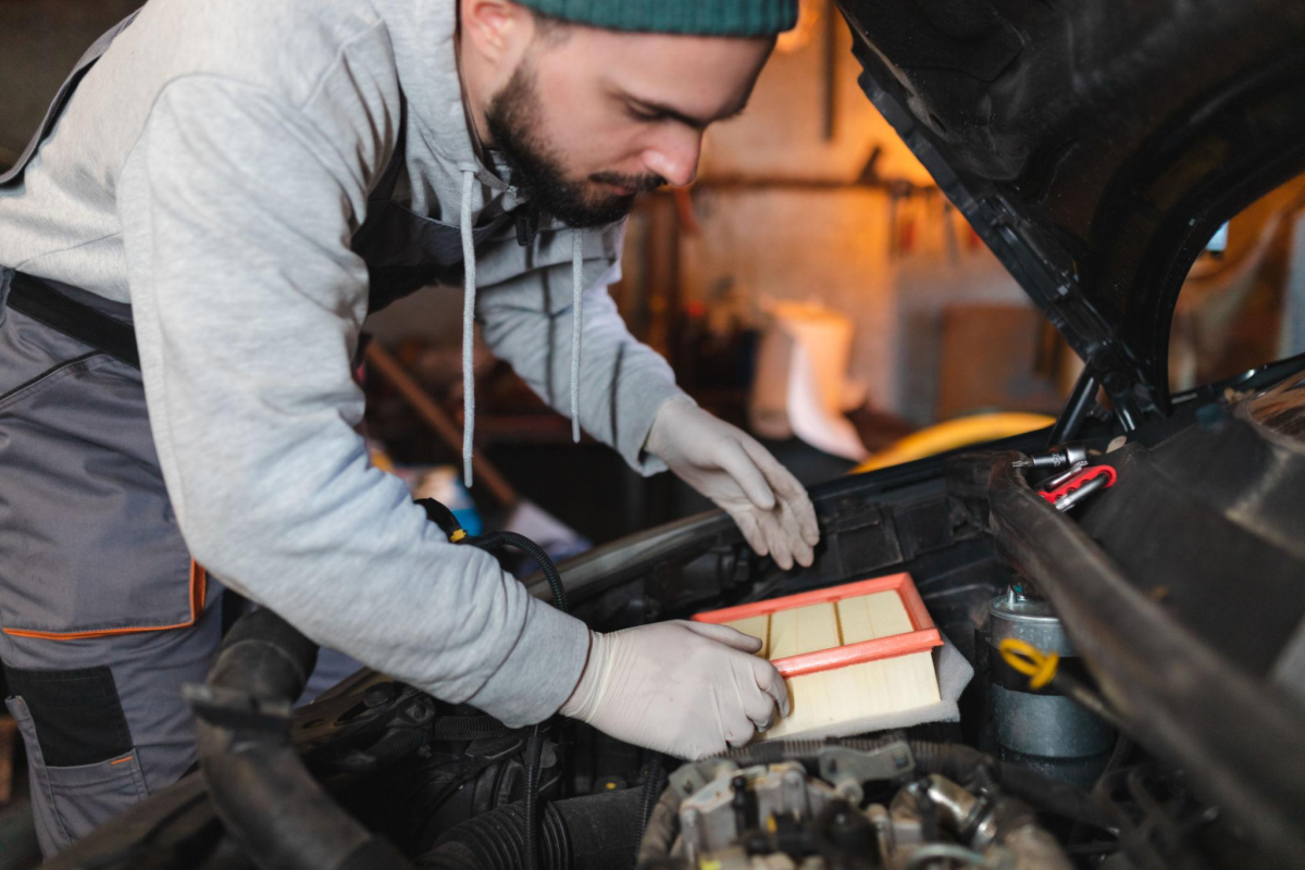 Mecânico verifica componentes do motor durante uma revisão preventiva em oficina.
